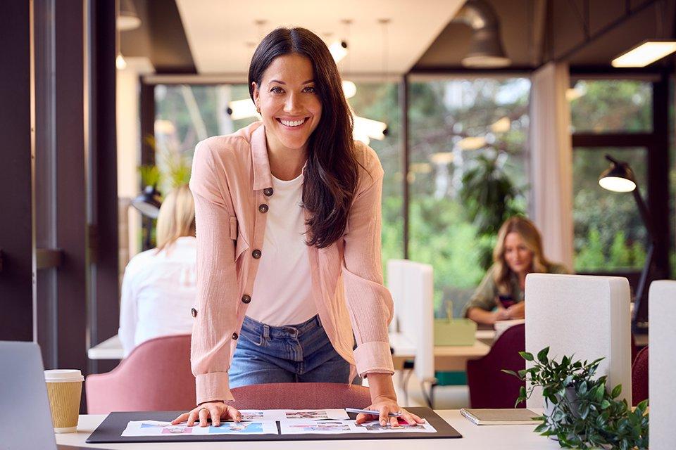 Female business administration professional smiles at camera while working at desk in office setting.